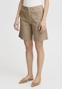Shorts en coton marron clair avec une coupe droite, des poches avant et une fermeture à bouton. Associés à des ballerines douces à bout rond.