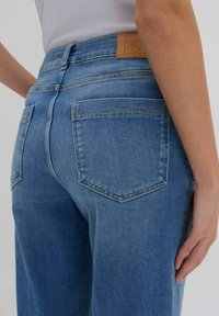 Jeans in denim azzurro chiaro con vita alta, dotati di due tasche posteriori, cuciture minime e un'etichetta in cuoio color beige all'altezza della vita.