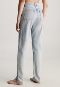 Svetle modré džíny rovného střihu s vysokým pasem, vybavené zadními kapsami a bočními rozparky na lemu. Denimový materiál s vybledlou texturou.