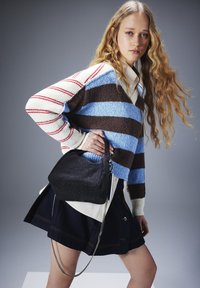 Sac à main noir structuré avec une texture douce, présentant une forme arrondie et une bandoulière en chaîne argentée. Porté avec un pull rayé multicolore.