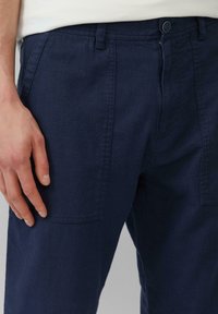 Marineblauwe, katoenen broek in een gemengde stof met een vlakke voorkant, rechte pijpen en zijzakken. Voorzien van een knoopsluiting en riemlussen.