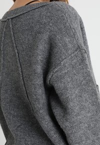 Szary sweter o luźnym kroju, szerokim dekolcie, ściągaczach w dół i miękkiej fakturze. Posiada detale szwowe wzdłuż pleców.