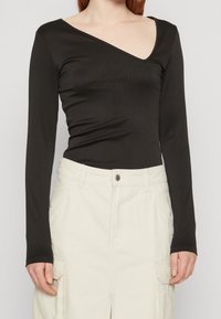 Černý žebrovaný body s dlouhým rukávem a hlubokým V-výstřihem, přiléhavý střih a hladký materiál, v kombinaci se smetanovou sukní typu cargo.