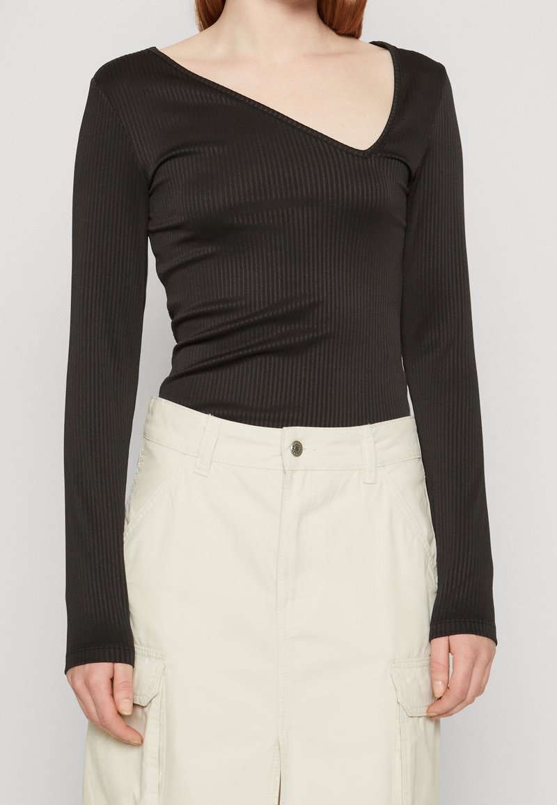 Černý žebrovaný body s dlouhým rukávem a hlubokým V-výstřihem, přiléhavý střih a hladký materiál, v kombinaci se smetanovou sukní typu cargo.