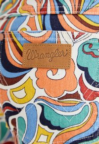 Tessuto di denim colorato e decorate con spirali e fiori in arancione, blu e verde; include un'etichetta in pelle marrone "Wrangler".