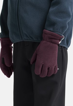 Guanti in pile di colore bordeaux scuro con una texture morbida, dotati di un polsino per il calore, indossati da una persona con una giacca in pile blu navy e pantaloni neri.