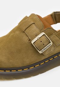Pantof verde din suede, slip-on, cu un detaliu metalic de tip cataramă, căptușeală moale și cusături galbene contrastante de-a lungul talpii.
