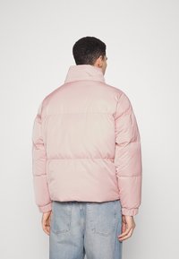 Vadderad rosa jacka med hög krage, elastiska ärmar och en fyrkantig silhuett, i kombination med lösa ljusblå denimjeans. Slät textur.