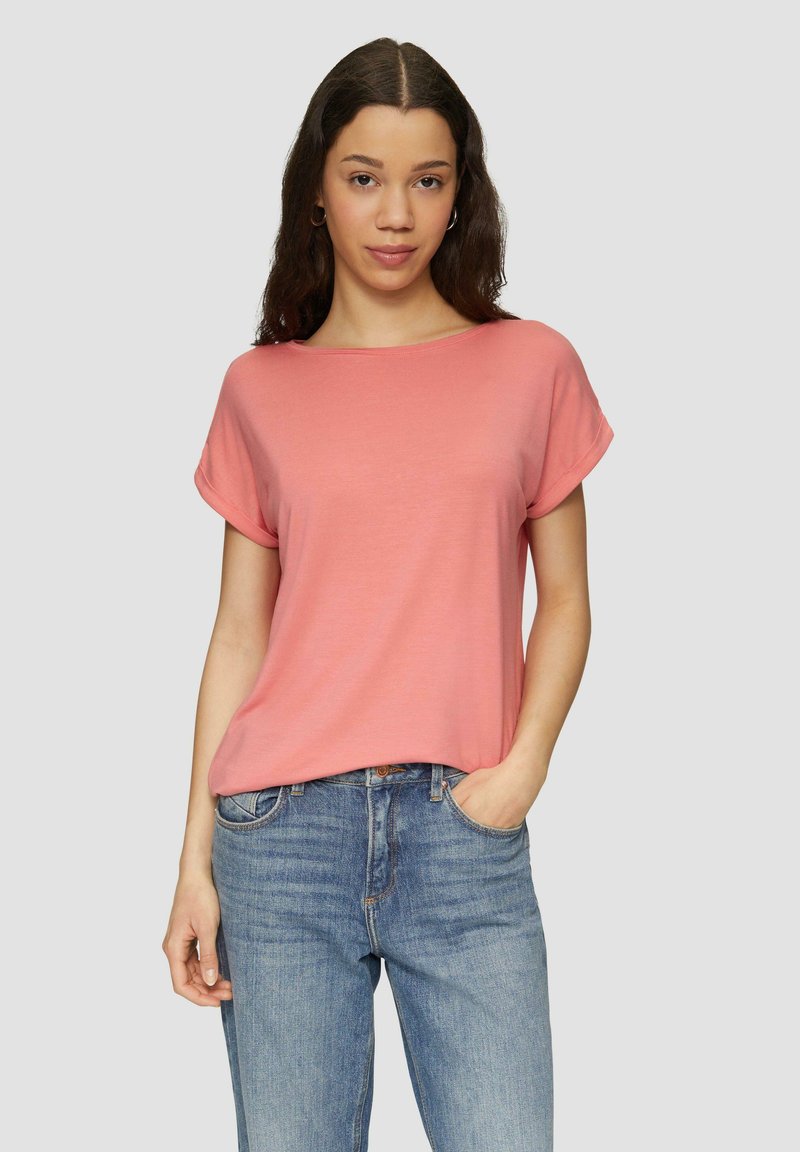 Bawełniany t-shirt z krótkim rękawem w kolorze koralowym, z okrągłym dekoltem i luźnym krojem. W zestawie z jasnoniebieskimi dżinsami o prostym kroju.