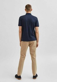 Námořnická polokošile s krátkým rukávem a klasickým límečkem, v kombinaci s béžovými kalhotami a tmavými botami. Jednoduchý design, hladká tkanina a přizpůsobený střih.