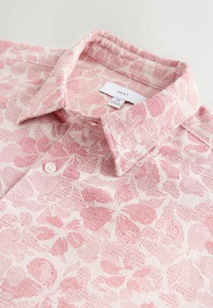 Lekka, wzorzysta koszula w odcieniach różu z kołnierzykiem, zapięciem na guziki i teksturowanym kwiatowym wzorem na jasnym tle. Widoczna etykieta markowa.