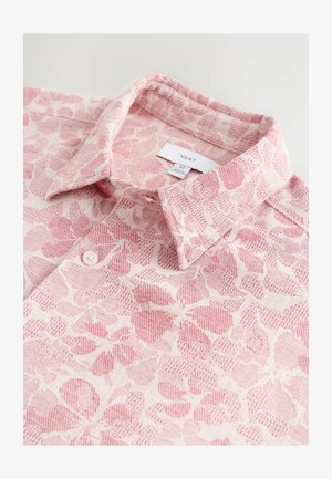 Lekka, wzorzysta koszula w odcieniach różu z kołnierzykiem, zapięciem na guziki i teksturowanym kwiatowym wzorem na jasnym tle. Widoczna etykieta markowa.