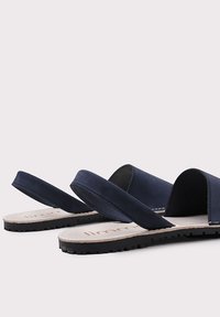 Marinefarbene Pantoletten mit zwei breiten Riemen, samtartiger Textur, flacher Gummisohle und kontrastierender beiger Innensohle mit Markennamen.