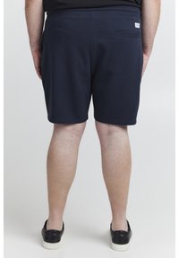 Dunkelblaue Baumwollshorts mit glatter Textur, elastischem Bund und einer einzelnen Gesäßtasche. Mit einem kleinen Logotag in der Nähe des Bundes.