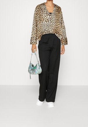 Mujer con blusa de estampado de leopardo, pantalones negros de cintura alta, zapatos blancos, sosteniendo un pequeño bolso plateado metálico con correa de cadena.