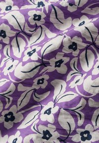 Lila szövet fehér és tengerészkék virágmintával. A textúra lágy és enyhén gyűrött, kiemelve a mintázat részleteit.