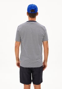 T-shirt a righe blu e bianche, maniche corte, scollo rotondo, abbinato a pantaloni corti scuri. Cappellino blu indossato al contrario.