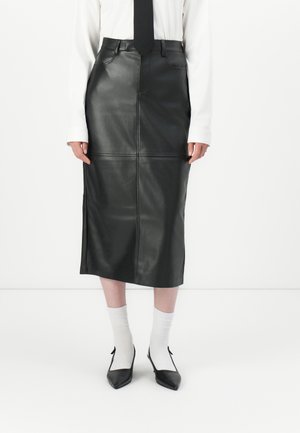 Sort læder midi-nederdel med en tætsiddende talje, forlommer og syninger. Styles med hvide ribbede sokker og sorte spidse sko.
