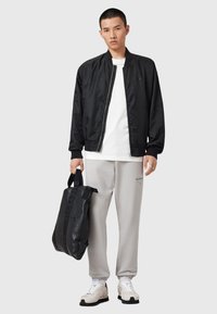 Zwarte bomberjack met ritssluiting, witte t-shirt, grijze joggingsbroek en zwarte tote bag. Witte sneakers met textuuropties.