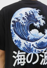 Camiseta de algodón negra con un gran gráfico de ola azul que presenta nubes blancas y texto japonés en la parte inferior, mostrando patrones detallados de agua.