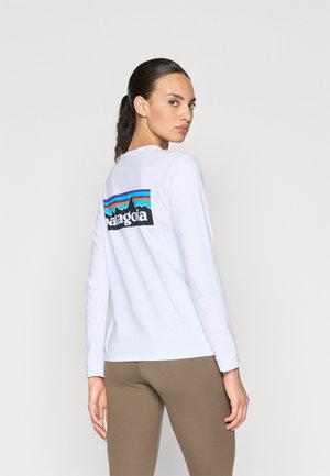 Langærmet hvid T-shirt lavet af bomuld, med et farverigt 'Patagonia' grafik på ryggen med bjerg- og stribedetaljer.