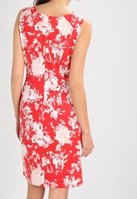 Czerwona sukienka w kwiaty z bezrękawowym fasonem. Posiada teksturowany materiał, żywe wzory białych kwiatów oraz dopasowany krój.