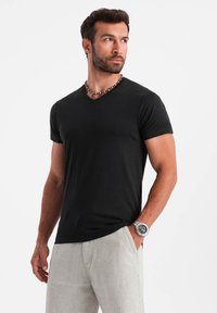Sort v-hals t-shirt i blødt stof, tætsiddende design med korte ærmer, parret med lyse bukser og perle-halskæde accenter.