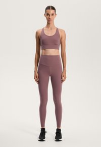 Mauve športni nedrček z širokimi naramnicami in brezšivnim dizajnom v kombinaciji z visokim pasom in legginsom. Obe obleki sta narejeni iz raztegljivega, gladkega materiala.