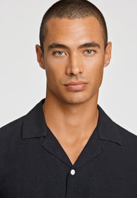 Σακάκι κοντομάνικο, σε σκούρο ναυτικό χρώμα, με κλασικό γιακά, διαθέτει κουμπωτή μπροστινή όψη και υφασμάτινη επιφάνεια με υφή. Λείος, σύγχρονος σχεδιασμός.