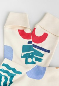 Chaussettes en crème douce avec des motifs abstraits colorés en rouge, bleu et vert. Style à revers avec une texture lisse et des designs graphiques distincts.