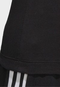 Svart bomullsidrottströja med en slät textur, försedd med en horisontell söm vid fållen och intill tre vita ränder.