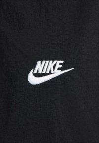 Svart t-skjorte i stoff med en brodert hvit Nike-logo midt på. Skjorten har en myk tekstur og en klassisk rund hals.