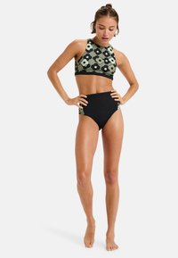 Bikini top s vysokým výstrihom s zeleným kvetinovým vzorom spárovaný s čiernymi nohavičkami s vysokým pásom. Hladká textúra, tesný strih a moderný dizajn.