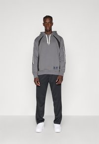 Grå huva sweatshirt med vita snörningar, svarta accenter och ränder; ihop med mörka byxor och vita sneakers. Enkelt atletiskt design.