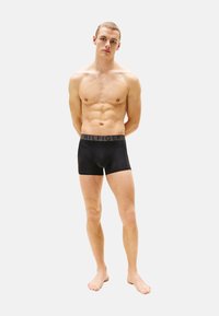 Boxer ajustados negros hechos de material elástico con una cinturilla con logo. Presenta un diseño ceñido y una longitud hasta el muslo. Textura suave.