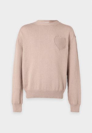 Mannequin masculin portant un pull beige avec un cœur texturé sur la poitrine, jean bleu et baskets blanches, debout avec une main dans la poche.