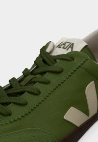 Πράσινο πάνινο αθλητικό παπούτσι με υφασμάτινη υφή, πράσινα κορδόνια και πατζάκι με λογότυπο σε κρεμ απόχρωση με μπεζ λεπτομέρεια στο πλάι.