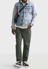 Chaqueta vaquera con sudadera con capucha gris, pantalones verdes, zapatillas negras. Incluye botones, bolsillos y un bolso cruzado. Conjunto casual en capas.