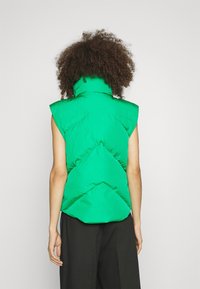 Groene mouwloze puffer-vest met hoge kraag, voorzien van een glanzende, doorgestikte textuur en een geometrisch ontwerp op de achterkant.