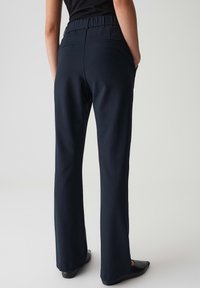 Marineblauwe uitlopende broek met een elastische tailleband, twee achterzakken en een soepele stofstructuur. Geschikt voor casual of semi-formele gelegenheden.