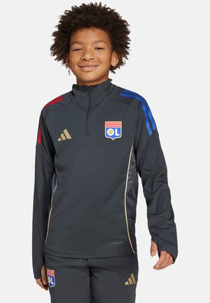 Veste d'entraînement zippée noire avec des rayures bleues et rouges sur les épaules, accents dorés et logo de l'Olympique Lyonnais. Présente une coupe athlétique et des manches longues.