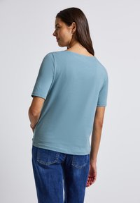 Lichtblauw kortgekapt shirt van zacht materiaal, met een ronde halslijn en een ontspannen pasvorm. Gepaard met blauwe spijkerbroek.