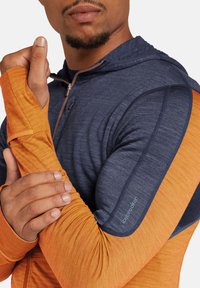 Lange mouwen sporttop met marineblauw en oranje kleurblokken, duimopening in de mouwen en een ritskraag, gemaakt van lichte, gestructureerde stof.