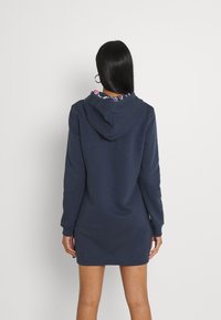 Vestido sudadera con capucha en color azul marino y mangas largas. Presenta un forro colorido y estampado en la capucha. Textura suave con un ajuste casual.