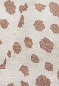 Breien stof met een roomkleurige achtergrond en onregelmatige bruine vlekken in verschillende maten, die een gladde textuur en een minimalistisch patroon toont.