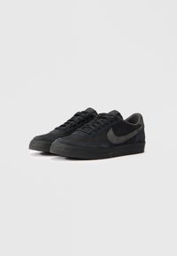 Melnas zamšādas sporta kurpes ar struktūru, ar tumšu „swoosh” logo, plakaniem šņorēm un gumijas zoli. Klasisks zema profila dizains.