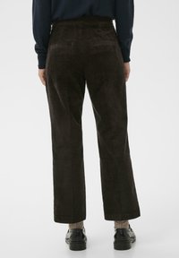 Pantalons en velours côtelé marron avec une coupe large, dotés de poches arrière et d'une surface texturée. Les pantalons se terminent juste au-dessus des chevilles.