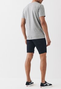 Grå kortærmet t-shirt lavet af blødt stof, parret med sorte denimshorts rullet ved kanten, med sidelommer og diskret syning.
