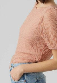 Hellrosa strukturiertes Oberteil mit kurzen Ärmeln, mit einem geknitterten Design und rundem Ausschnitt, getragen zu hoch taillierten Jeans.