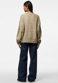 Överdimensionerad beige tröja med texturerad stickning, med ett ribbat nederkant och ärmslut. I kombination med mörkblå vida jeans.